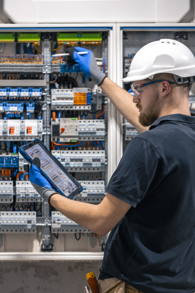 Electrical technician working in a switchboard with fuses, uses a tablet. Electrical technician looking focused while working in a switchboard